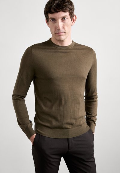 Olijfgroene trui met ronde hals, gemaakt van zachte stof, met lange mouwen en geribbelde manchetten. Gecombineerd met donkere broek.