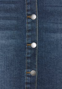 Jupe en denim à boutons sur le devant, fabriquée dans un tissu bleu foncé, dotée de boutons en métal argenté et de coutures jaunes contrastantes le long des coutures.