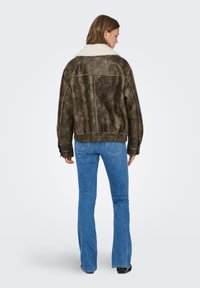 Καφέ μπουφάν από συνθετικό δέρμα με λευκή συνθετική γούνα στο γιακά, oversized εφαρμογή, ελαστική ζώνη στη μέση και λεπτομερείς ραφές, φορεμένο με τζιν καμπάνα.