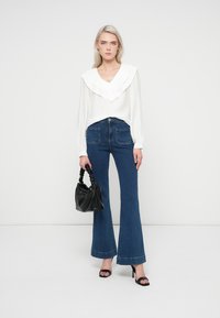 Hvid bluse med flæsekrave, parret med blå vide jeans. Sort håndtaske med snoet håndtag og open-toe hæle sandals.