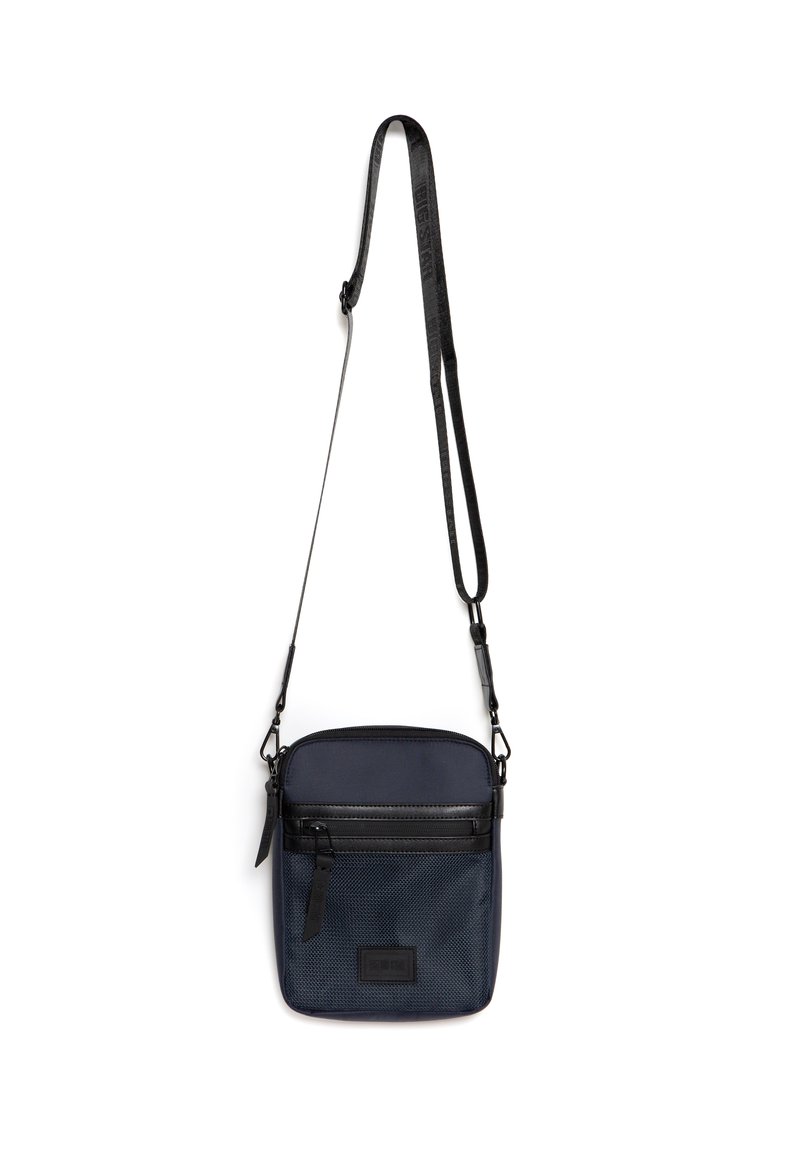 Námořnická nylonová taška přes rameno s černým zipem, přední kapsou a nastavitelným popruhem. Texturovaný povrch s obdélníkovým tvarem a detailem loga.