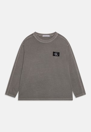 Grå langærmet crewneck-sweatshirt med sort Calvin Klein Jeans logo-patch på venstre bryst, lagt fladt på hvid baggrund.
