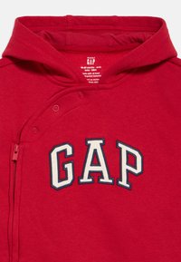 Rode babyhoodie met ritssluiting en drukknoopjes aan de voorkant, met "GAP" in grote witte en marineblauwe letters op de borst.