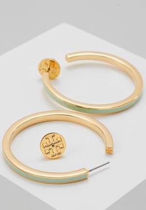 Boucles d’oreilles créoles ton or avec détail émaillé bleu clair et clous circulaires gravés du logo sur une surface blanche.