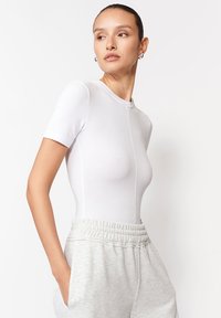 Biały body z krótkim rękawem o dopasowanym kroju, bezszwowej strukturze i okrągłym dekolcie, w zestawie z szarymi spodniami dresowymi ze sznurkiem.