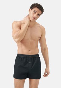 Svarta korta boxerkalsonger med elastisk midja, detalj med knapp framtill och slät tygkvalitet. Modellen är utan tröja och visar passformen.