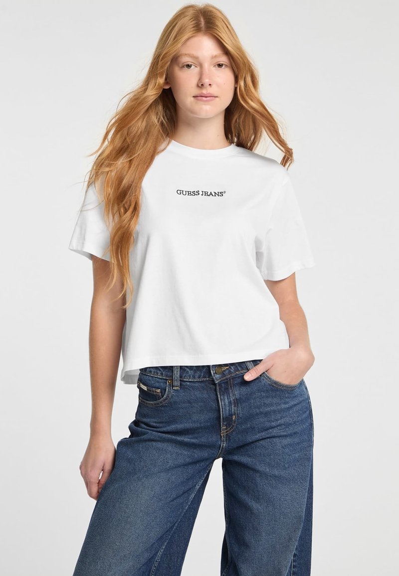 Valge lühike t-särk, mis on valmistatud puuvillast ja millel on must "GUESS JEANS" logo. Sobib kõrge vöökohtadega tumedate siniste teksadega. Sujuv tekstuur.