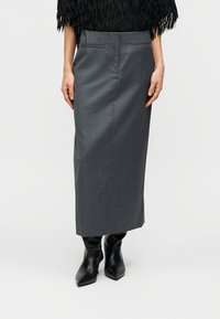 Jupe crayon grise sur mesure avec ceinture, poches latérales et texture lisse, assortie à des bottines noires à bout pointu.