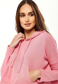 Light pink hoodie with a drawstring and kangaroo pocket. Soft texture, long sleeves, and ribbed cuffs highlight its casual design.