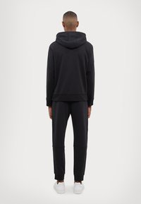 Black hoodie and matching joggers made from soft fabric. Hoodie features a large hood, and joggers have elastic cuffs. White sneakers complete the look.