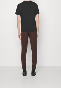Svart kortärmad t-shirt parat med mörkbruna slim-fit byxor och svarta skor, stående mot en neutral bakgrund.