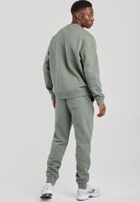 Felpa e pantaloni jogging in verde tenue. Combinazione di cotone morbido, collo a girocollo, polsini a coste e vita elastica. Dettaglio con tasca posteriore sui pantaloni.