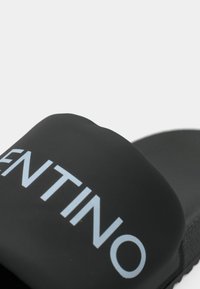 Zwarte schuif sandaal met een matte afwerking, voorzien van een groot merklogo in lichtblauw en een gestructureerde zool voor grip.