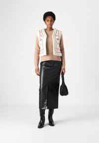 Knit beige sweater layered with a cream vest featuring pink embroidered stars. Black leather midi skirt with slit. Black textured handbag.