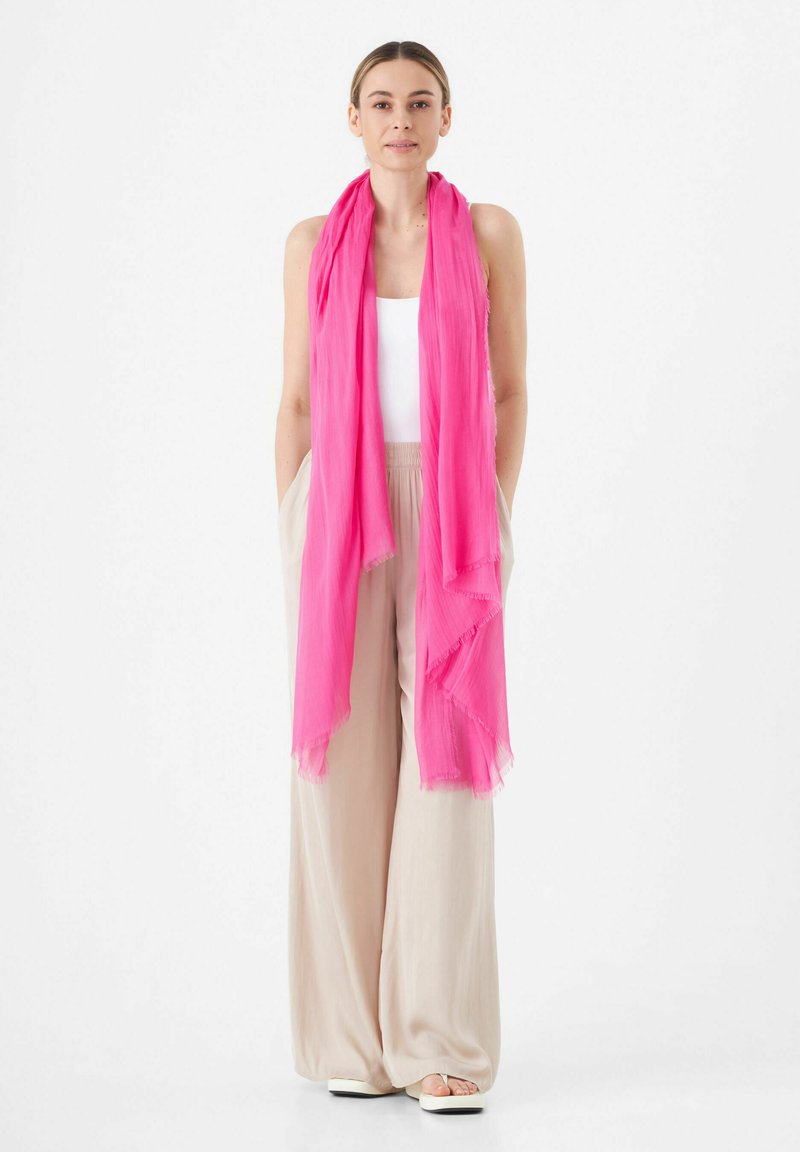 Roze chiffon sjaal met een lichtgewicht, luchtig ontwerp en rafelige randen, casual om de nek gedrapeerd, gecombineerd met beige wijde broekspijpen.
