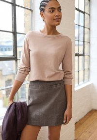 Light pink long-sleeve top paired with a gray checked mini skirt, featuring front pockets and a soft texture. Model holds a dark jacket.