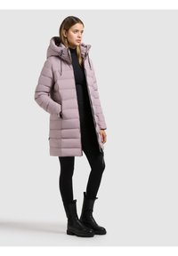 Lichtpaars, doorgestikt donsjack met capuchon, ritssluiting aan de voorkant en zijzakken; gedragen over zwarte legging en zwarte laarzen.