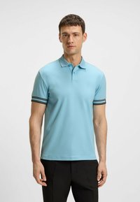 Hellblaues Polohemd mit Kragen und kurzen Ärmeln, das mit schwarz-weißen Streifen verziert ist, aus glattem Stoff gefertigt und kombiniert mit schwarzen Hosen.