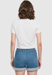 T-shirt blanc à manches courtes associé à un short en denim bleu, avec des revers aux poignets et des poches arrière, vu de dos.