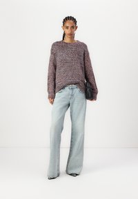 Chunky strikkegenser i lilla og blå nyanser, parret med lyseblå vide jeans. En svart veske og elegante svarte sko fullfører antrekket.