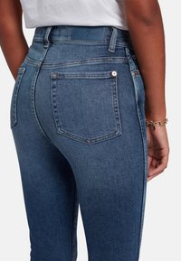 Jeans in denim blu a vita alta con una texture liscia, caratterizzati da due tasche posteriori e una patch in pelle in vita, progettati per una silhouette aderente.