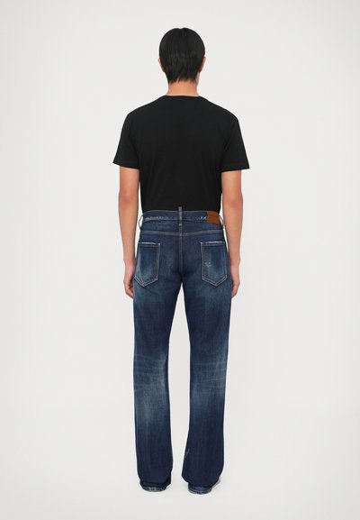 Camiseta negra y jeans de denim azul vistos desde atrás. Los jeans tienen un ligero desgaste, dos bolsillos traseros y un parche de cuero marrón en la cintura.