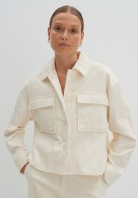 Cremfarbener Cordjacke mit zwei Fronttaschen, einem Knopfverschluss und einem Kragen. Verfügt über eine gerippte Textur und ein kurzes Design.