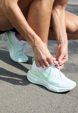 Persoon hurkend op het trottoir terwijl hij witte en lichtgroene veters van sportschoenen strikt.