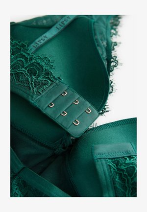 Smaragd zöld csipkebrá, átlátszó részletekkel, puha anyagból, finom díszítéssel és többlépcsős zárással, rézszínű hardverrel.