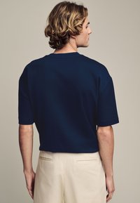 Camisa de manga corta color azul marino hecha de tela suave, con un ajuste relajado y un escote simple, combinada con pantalones crema con bolsillos traseros.