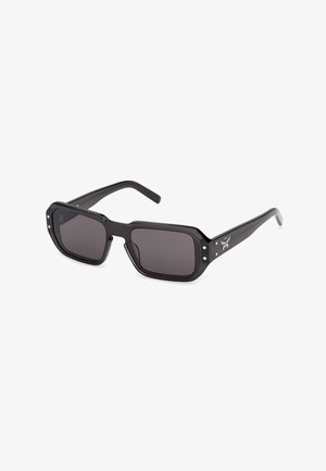 Gafas de sol rectangulares negras con lentes oscuras, montura gruesa y pequeños detalles blancos en forma de diamante cerca de las bisagras.