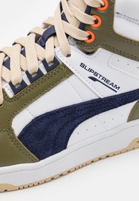 High-top sneaker with beige laces, olive green and white leather, navy suede stripe, and "SLIPSTREAM" branding on the side.