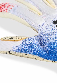 Gros plan sur un gant de sport blanc avec un tissu tricoté à motifs bleu et rouge et une paume beige doté d'une prise noire mouchetée, étiqueté "LMM Elite Dual Grip".
