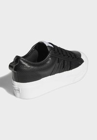 Černé syntetické kožené tenisky s perforovanými detaily, bílou gumovou podrážkou, zaoblenou špičkou a plochými černými tkaničkami. Jemný akcent na zadním tabulkovém dílu.