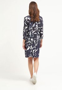 Vestito a fantasia floreale in blu navy con dettagli bianchi e blu, tessuto semi-trasparente, maniche a tre quarti, abbinato a sneakers bianche.
