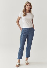 Camiseta blanca de manga corta combinada con pantalones azules ajustados. Los pantalones tienen bolsillos y una textura sutil. El calzado es una sandalia deslizante de color claro.
