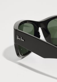 Ochelari de soare negri, unghiulari, cu lentile verzi, având o finisare lucioasă și un logo argintiu "Ray-Ban" pe lateral.