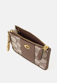 Portefeuille en cuir marron et toile, avec une fermeture éclair dorée, présentant un motif tissé et une chaîne détachable. Design compact avec un compartiment intérieur.