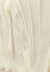 Lotion ou crème blanche lisse et crémeuse, étalée avec des crêtes douces visibles et une texture sur une surface plane.