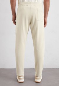 Beige joggingsbroek gemaakt van zachte stof, met een elastische tailleband en een enkele achterzak. Gepaard met lichtgekleurde sneakers.