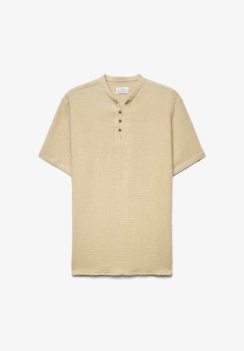 Chemise beige texturée à manches courtes avec un col rond et trois boutons marron sur une patte de boutonnage au centre avant.