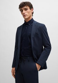 Marineblaues Anzug mit strukturiertem Stoff, kombiniert mit einem passenden Hemd mit Button-Down-Kragen und dezentem Logodetail, schlanke Passform.