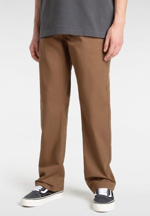 Brown cotton blend trousers with a straight leg design, paired with black and white sneakers featuring a textured canvas upper.