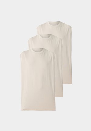 Trois débardeurs beiges unis à col rond empilés en diagonale sur un fond clair.