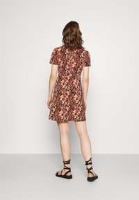 Robe courte à fleurs noire, rose et orange avec manches courtes et taille ajustée, associée à des sandales noires à brides sur des pieds nus.