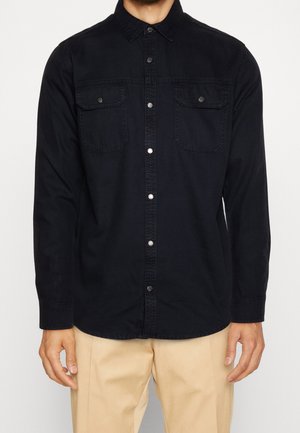Zwarte overhem shirt met lange mouwen, twee borstzakken, drukknoopsluiting en een zachte textuur, gecombineerd met beige broeken.