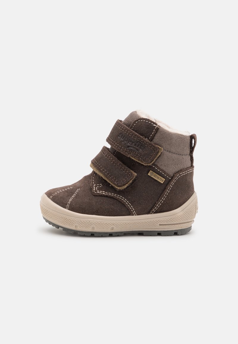 Botte bébé en daim marron avec semelle en caoutchouc beige, double fermeture Velcro, étiquette Gore-Tex et doublure intérieure douce couleur crème.