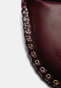 Burgundy leather bag with gold-tone hardware, featuring decorative lacing along one edge. Smooth texture with a structured shape.