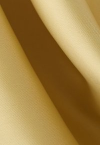 Miękka beżowa tkanina o delikatnej skośnej fakturze splotu, ułożona w gładkie fałdy tworzące kontrasty światła i cienia.