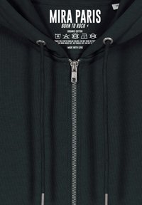 Felpa con cappuccio in cotone biologico di colore verde scuro. Presenta una zip YKK silver, lacci e un'etichetta stampata con le istruzioni per la cura.